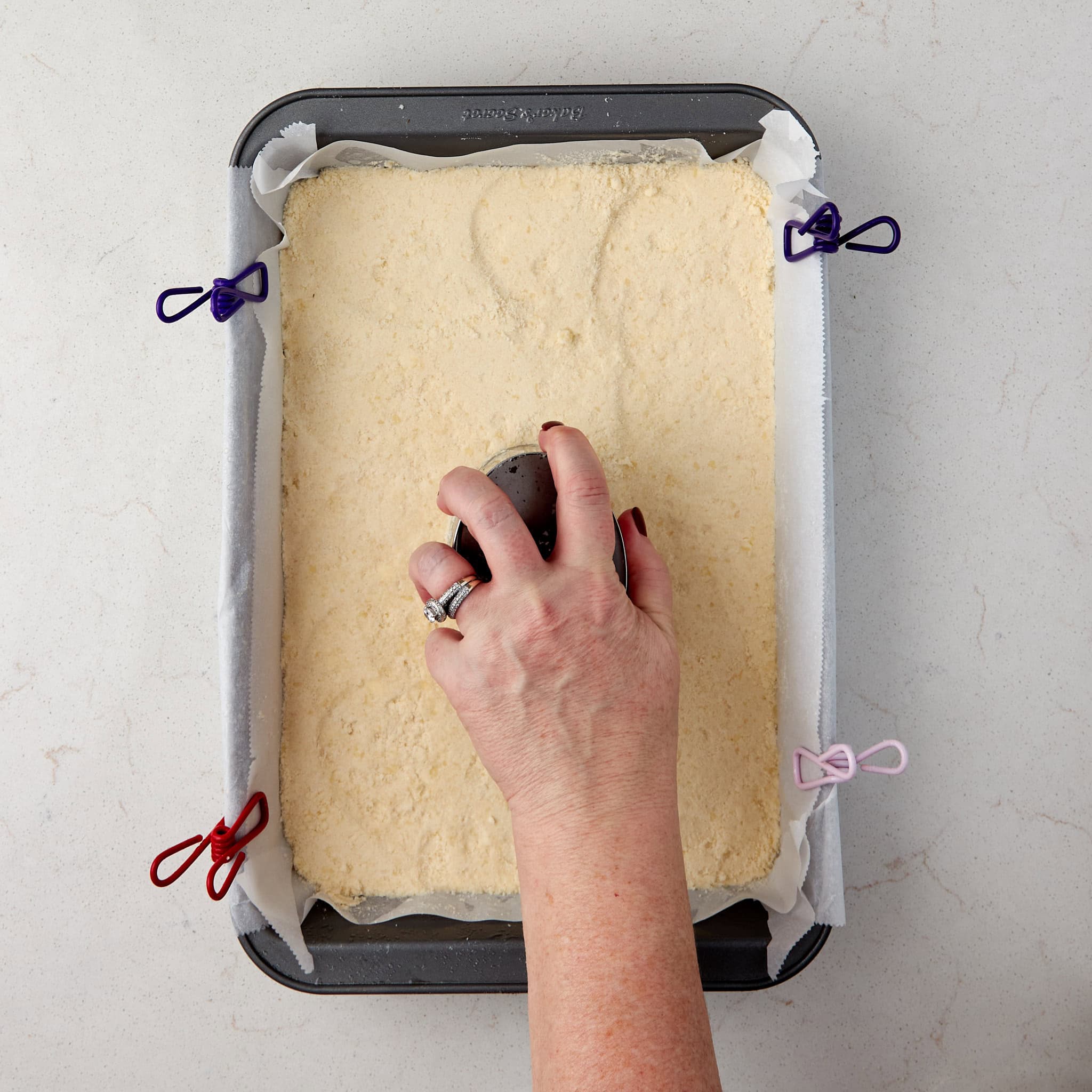 shortbread crust being pressed into a baking pan with the bottom of a measuring cup.