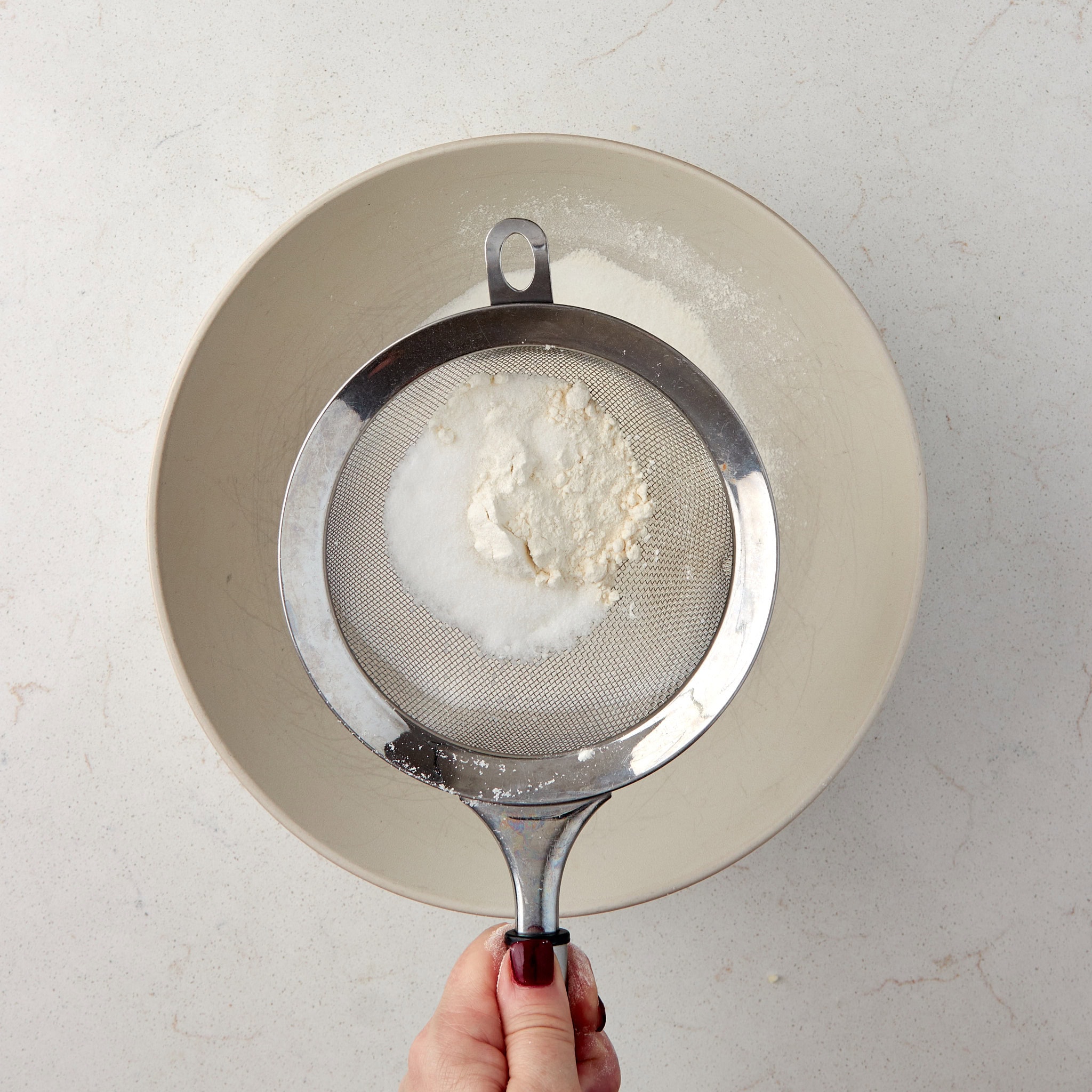 sugar and flour being sifted into a bowl.