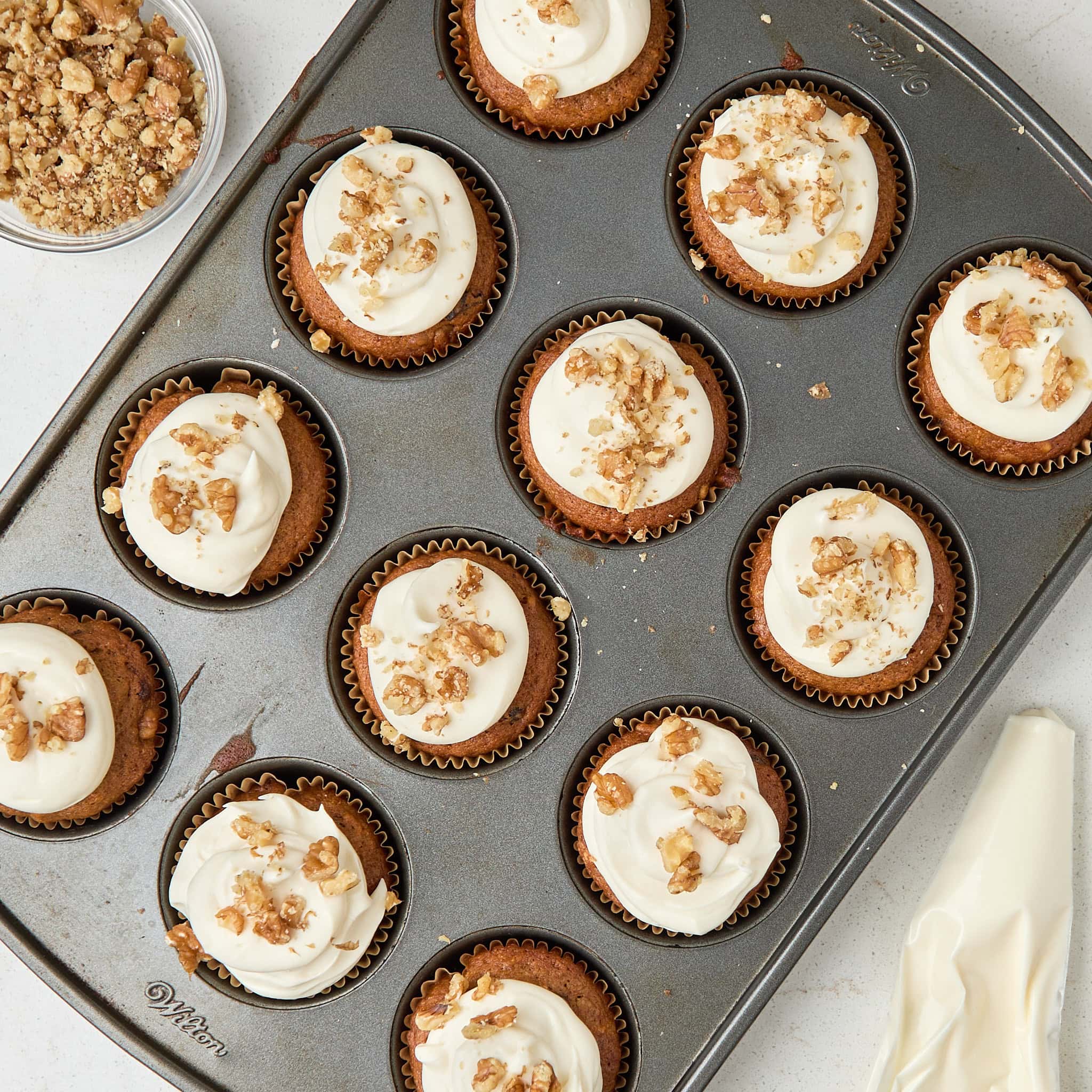 cooked muffins in a muffin tin topped with cream cheese frosting and walnuts