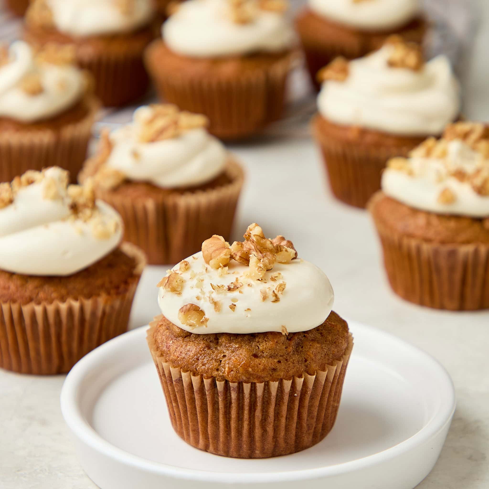 carrot cake muffin with cream cheese frosting topped with walnuts sitting on a white plate.
