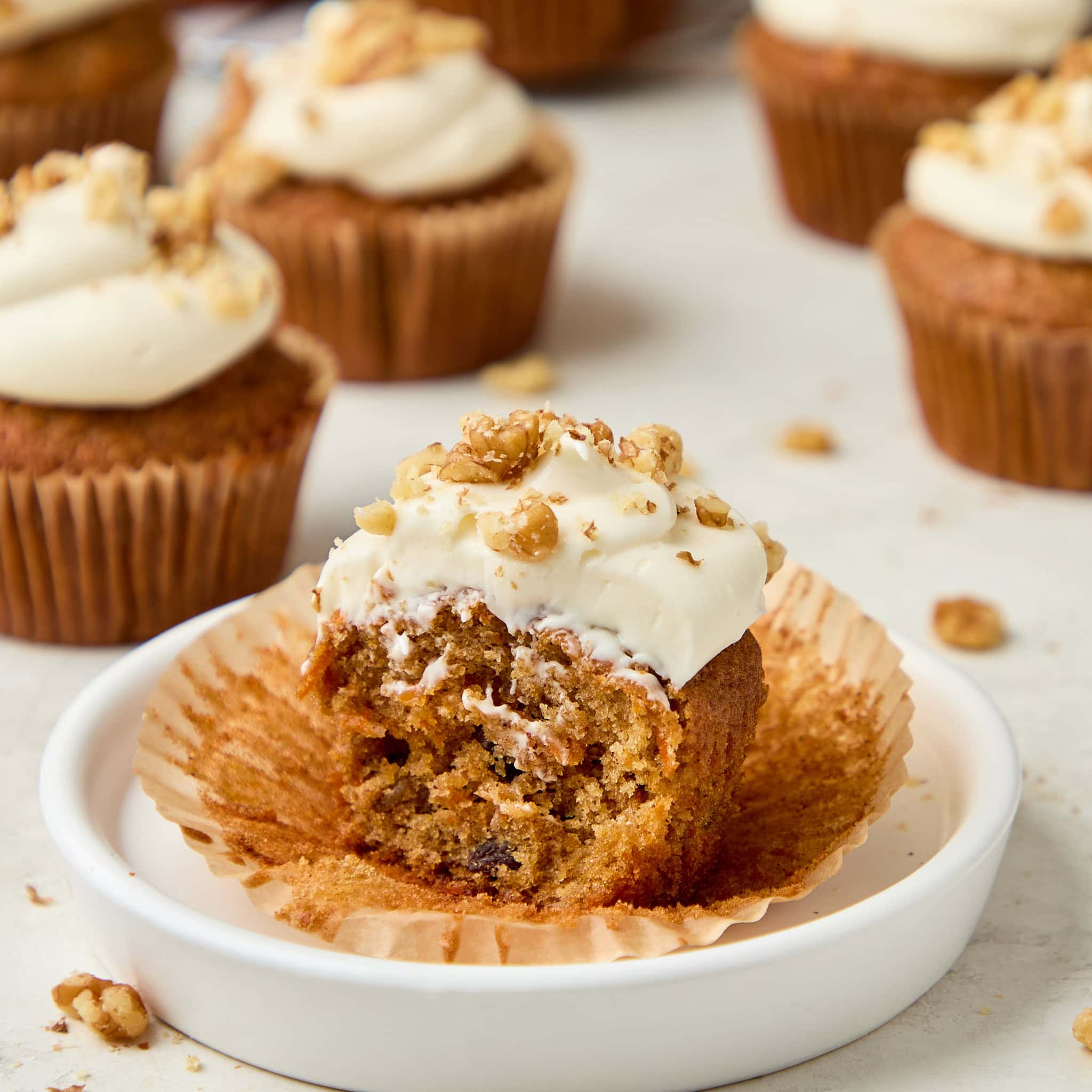 carrot cake muffin with cream cheese frosting topped with walnuts with a bite missing.