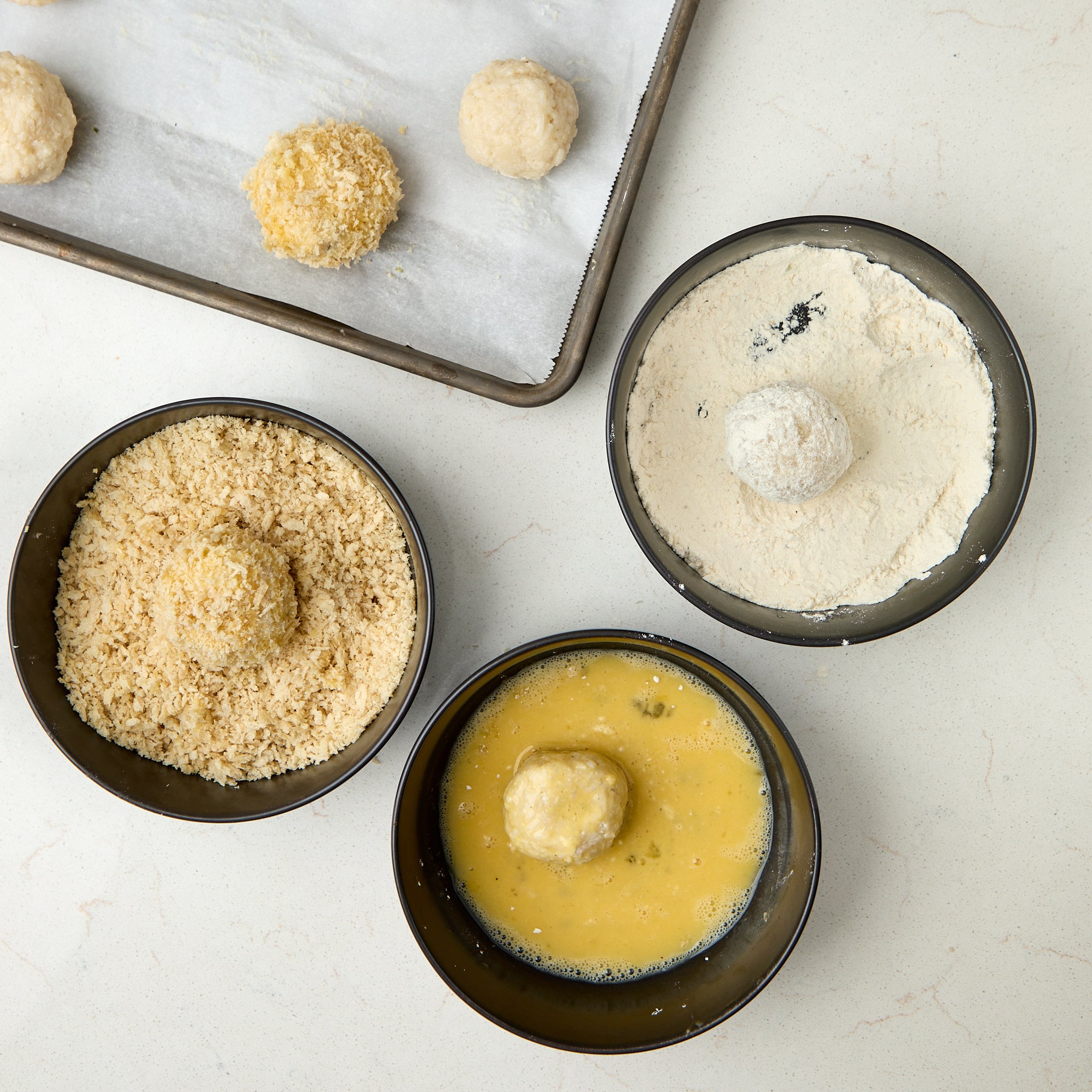 arancini balls being dredged in flour, egg, and bread crumbs.