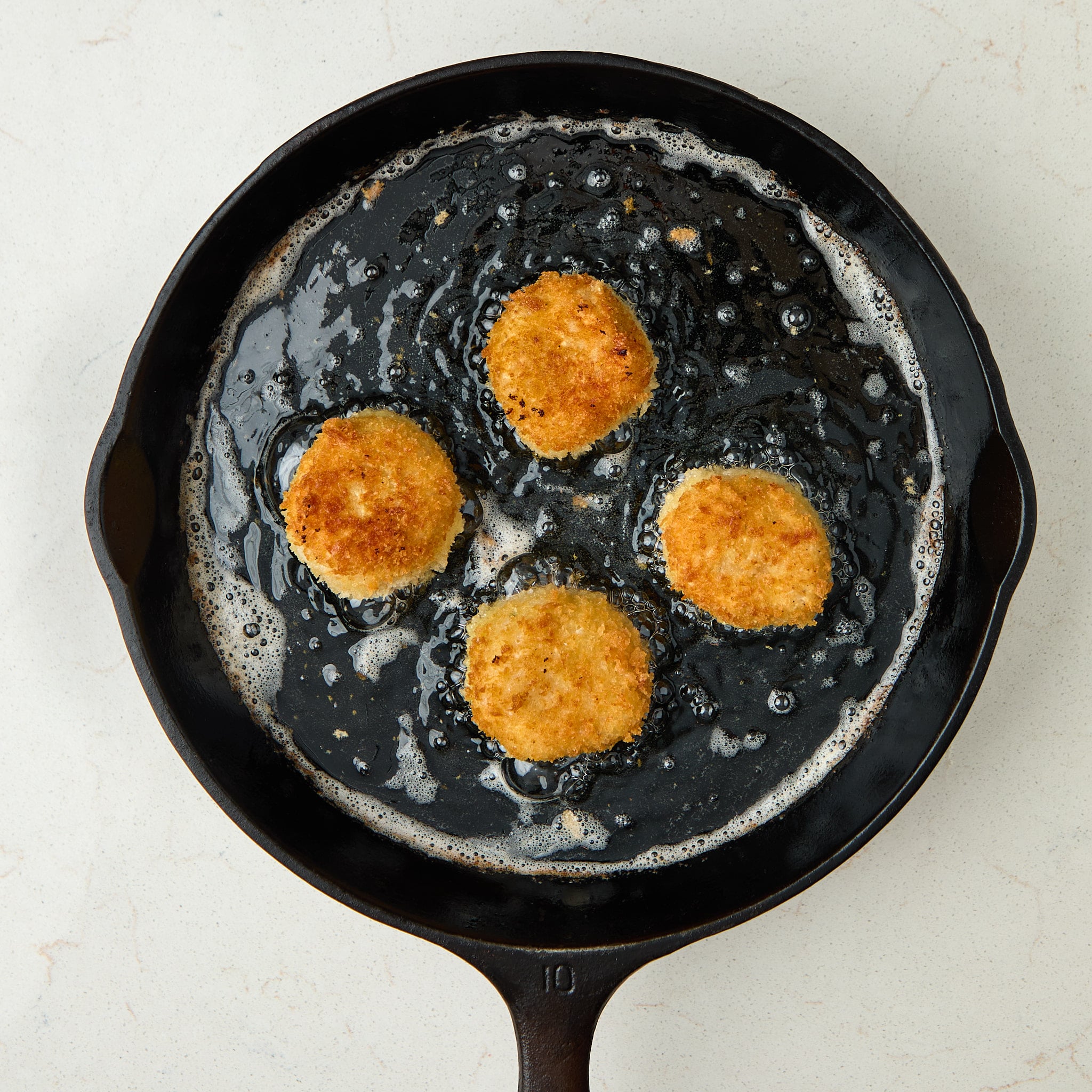 risotto balls being fried in a cast iron pan.