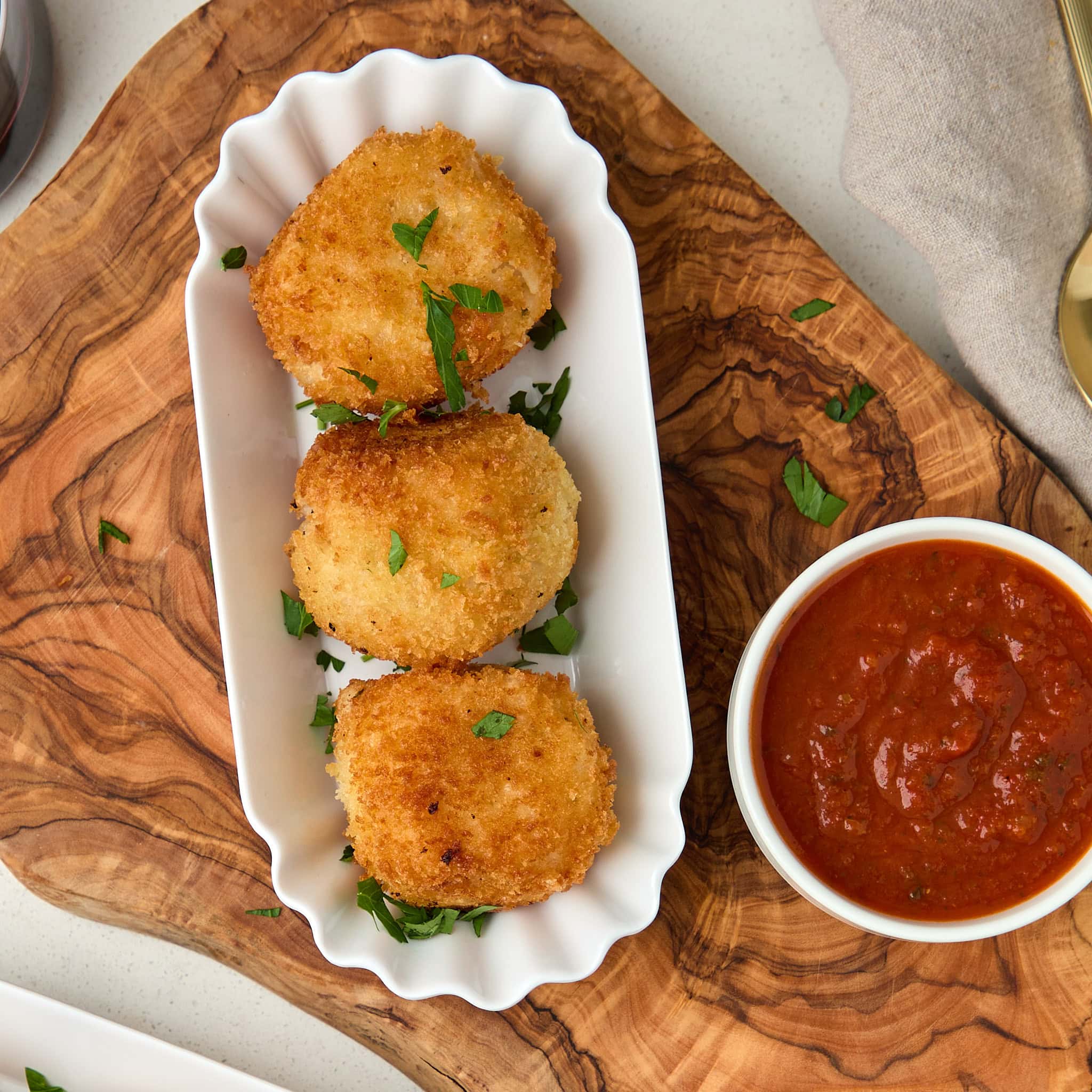 3 arancini risotto balls divided in a white platter with marinara sauce.