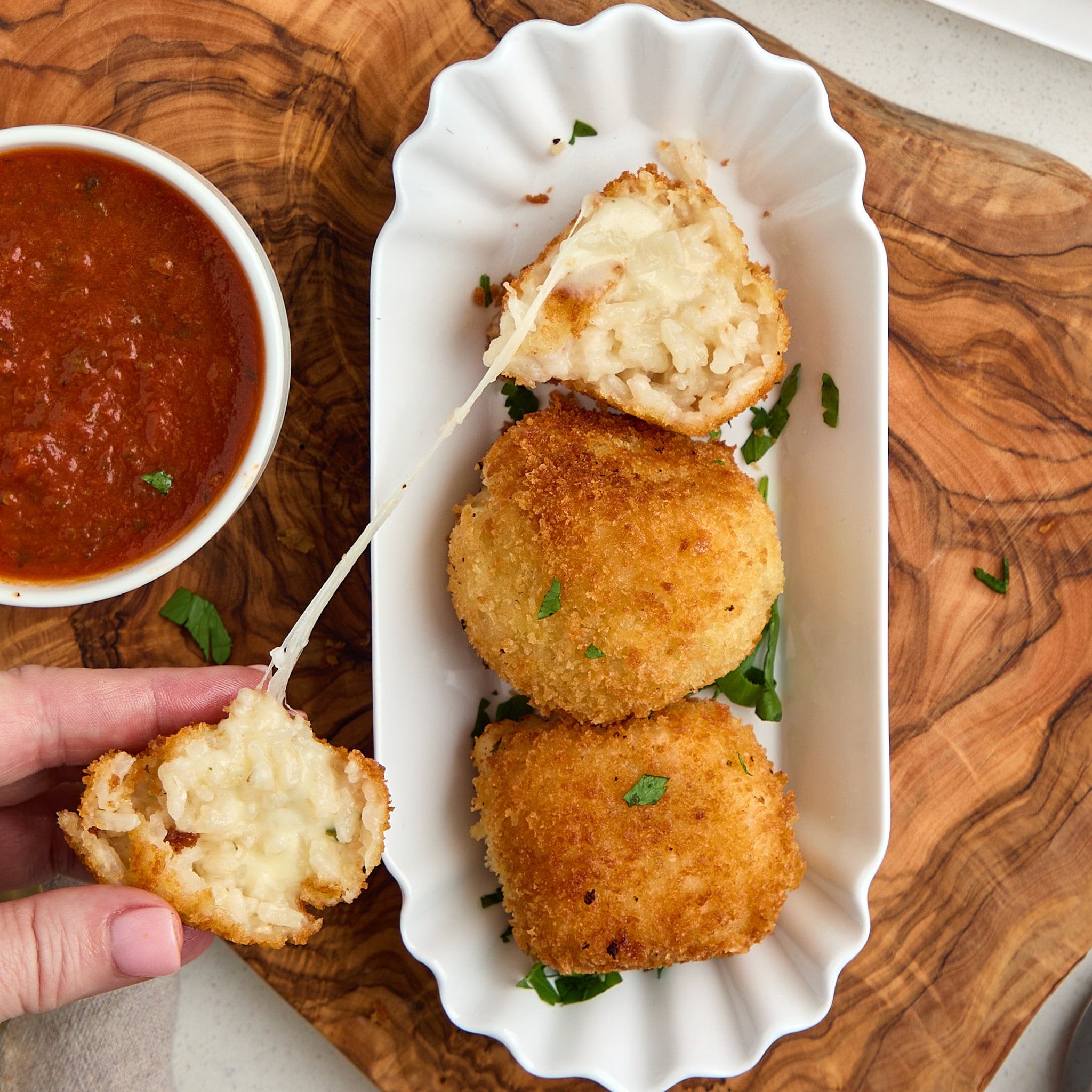 3 arancini in white platter and one is cut in half creating a cheese pull.